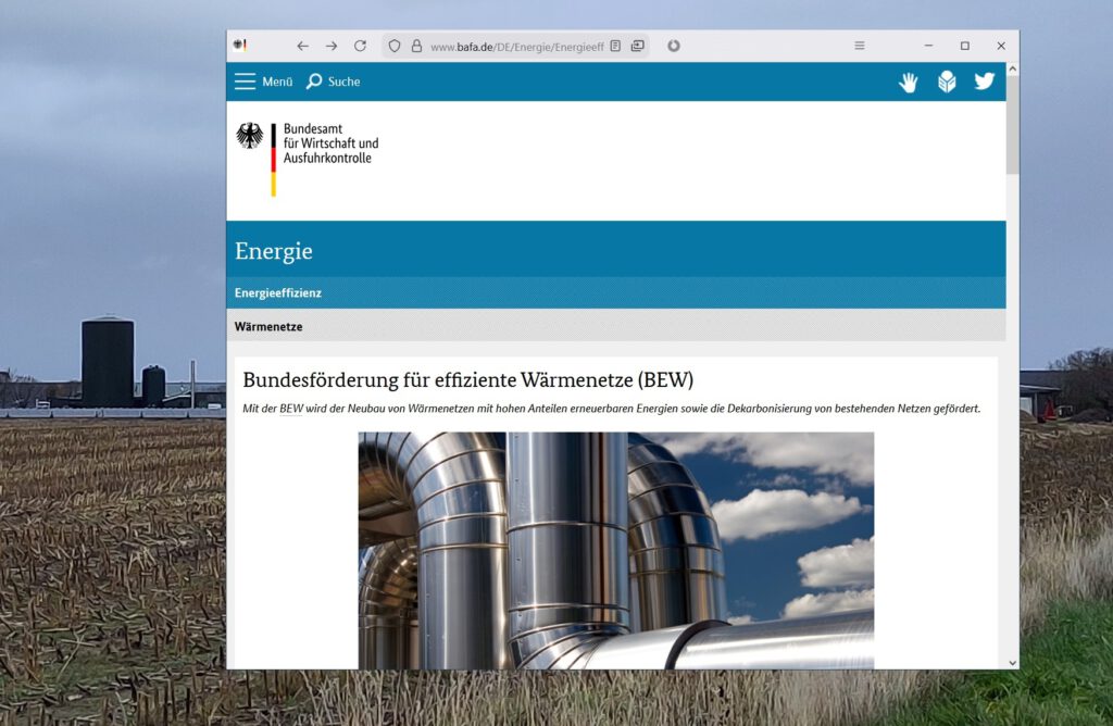 Im Hintergrund ist die Heizzenbtrale Oldsum mit Solarthermiefeld und Wärmespeicher zu erkennen. Rechts im Vordergrund ist die Webseite zur Bundesförderung für effiziente Wärmenetze (BEW) geöffnet.